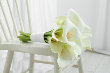 Beautiful calla lily flowers tied with ribbon on white chair indoors