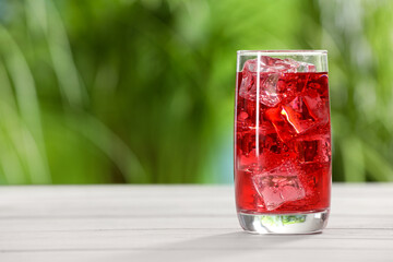 Glass of refreshing soda water with ice cubes on white table outdoors, space for text