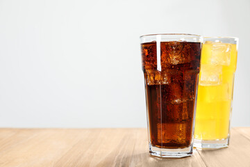 Glasses of different refreshing soda water with ice cubes on wooden table, space for text