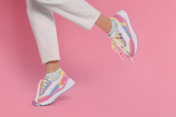 Woman wearing pair of new stylish sneakers on pink background, closeup