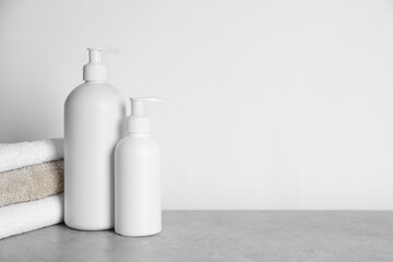 Bottles of cosmetic products and towels on grey table. Space for text