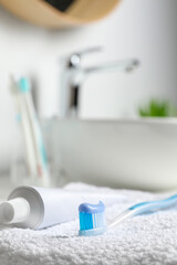 Plastic toothbrush with paste and tube on white towel in bathroom, closeup. Space for text