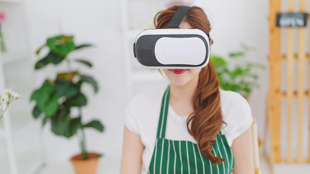 Young asian women owner floral store wearing VR glasses for working and select flowers through virtual reality headset. Business and technology concept, Metaverse virtual