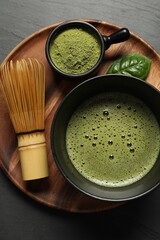 Cup of fresh matcha tea, bamboo whisk and green powder on black table, top view