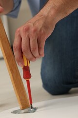 Man with screwdriver assembling furniture on floor, closeup