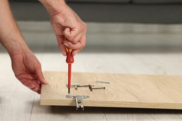 Man with screwdriver assembling furniture on floor indoors, closeup. Space for text