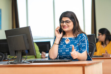 Indian woman showing thumps up while working on computer at office.