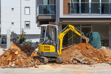 Excavator works dug trenches next to a residential building under construction for laying communications