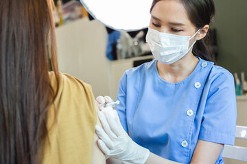 Female doctor wearing mask holding syringe giving vaccinations to patient for protection. During...