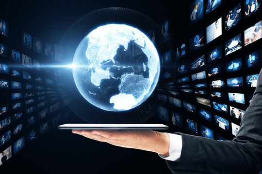 Close up of businessman hands holding tablet with creative glowing polygonal globe with rows of images on dark background. Connecting businesspeople, video conference concept.