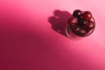 Close up of glass of red grapes and copy space on pink background