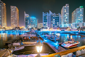 Dubai Marina Port, UAE, United Arab Emirates - Night view of high-rise buildings of residential district in Dubai Marina And Yachts Moored Near Pier In Evening Night Illuminations.
