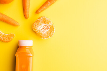 Close up of bottle with juice, carrots and tangerines with copy space on yellow background