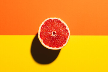 Close up of half of red grapefruit and copy space on orange and yellow background