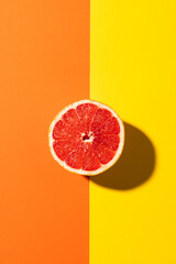 Close up of half of red grapefruit and copy space on orange and yellow background