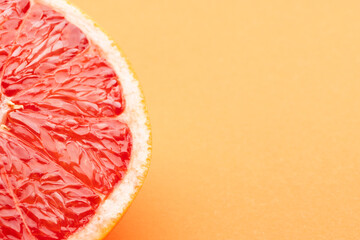 Close up of half of red grapefruit and copy space on orange background