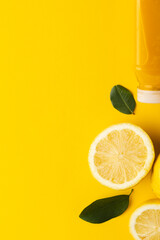 Close up of bottle with juice, lemon, lemon slices and leaves with copy space on yellow background