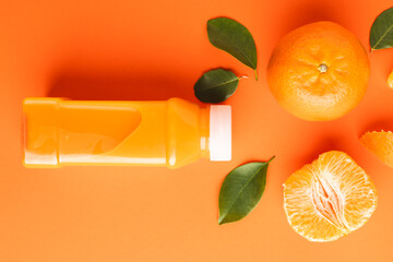 Close up of bottle with juice, tangerine, segments and leaves with copy space on orange background