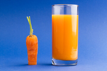 Close up of carrot and glass of carrot juice with copy space on blue background