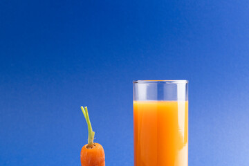Close up of carrot and glass of carrot juice with copy space on blue background