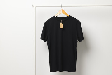 Naklejka premium Black t shirt with tag hanging from clothes rack with copy space on white background