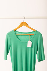 Fototapeta premium Green t shirt with tag on hanger hanging from clothes rail with copy space on white background