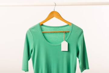 Green t shirt with tag on hanger hanging from clothes rail with copy space on white background