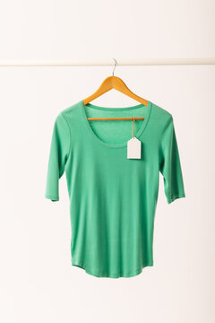 Green t shirt with tag on hanger hanging from clothes rail with copy space on white background