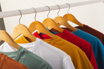 Naklejka premium Multi coloured t shirts on hangers hanging from clothes rail and copy space on white background