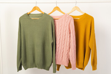 Naklejka premium Three sweaters hanging from clothes rail with copy space on white background