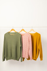 Naklejka premium Three sweaters hanging from clothes rail with copy space on white background