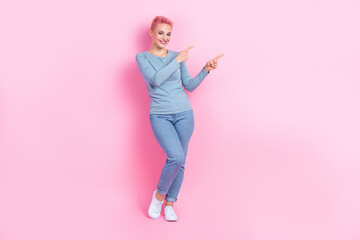 Full size photo of friendly girl dressed blue sweatshirt denim pants indicating at empty space sale isolated on pink color background