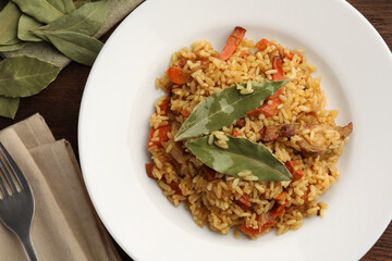 Delicious pilaf, bay leaves and fork on wooden table, flat lay