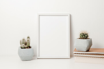 Photo frame mockup with cactuses in pots, books and notepads on white table. Photo frame template with copy space for design, poster or picture, aesthetic home decoration, cozy scandinavian style