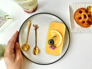 Woman's hand holding a plate with a dessert lemon cheese tart on a white plate wooden table background 