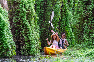 Asian woman wearing a hat comes on a kayaking adventure with her mother in a lake with a natural view into the forest. Concept family trips and water sports adventure activities.