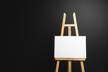 White canvas on wooden easel and copy space on black background