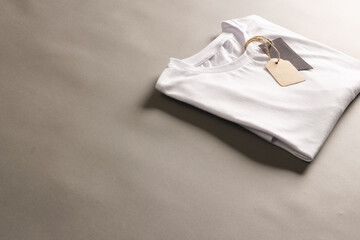 Folded white t shirt with tags with copy space on brown background