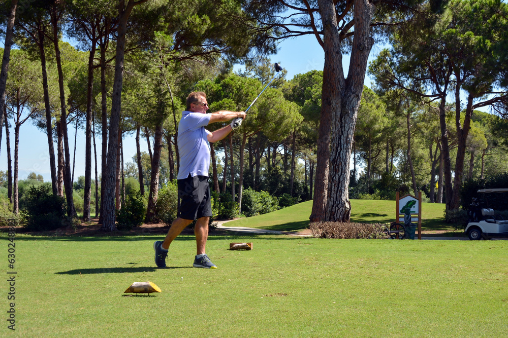 Wall mural a caucasian male hits a golf ball near the hole on the green of a private golf club. golf cart and p