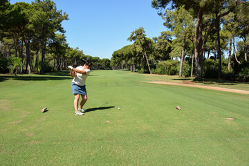 Fototapeta premium A young Caucasian woman hits a golf ball near the hole. In the background, in the perspective, is the glade of a private golf club. Active summer luxury vacation