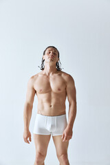 Portrait of handsome man with braids, muscular strong body standing shirtless in underwear against grey studio background. Concept of men's beauty, body care, sport, wellness, healthy lifestyle, ad