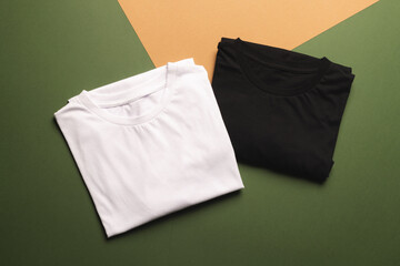 Close up of folded white and black t shirts and copy space on green to orange background
