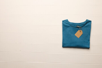 Close up of flat lay of blue t shirt with tag and copy space on white boards background