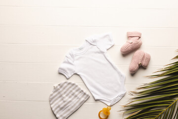 Flat lay of white baby grow, hat, dummy and pink booties with copy space on white background