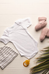 Flat lay of white baby grow, hat, dummy and pink booties with copy space on white background