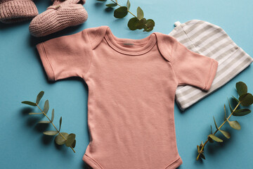 Flat lay of orange baby grow, hat and pink booties with copy space on blue background