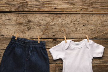 White baby grow and denim shorts hanging with clothes pegs with copy space on wooden background