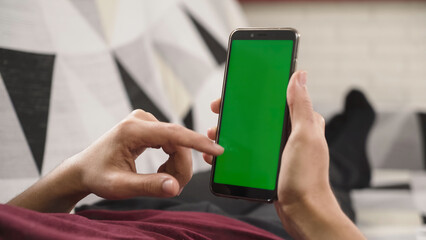 Person holding a mobile phone with a green screen, ready to replace it with any content