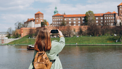 Beautiful stylish woman in hat walking in Krakow on autumn day and holding mobile phone. Urban...