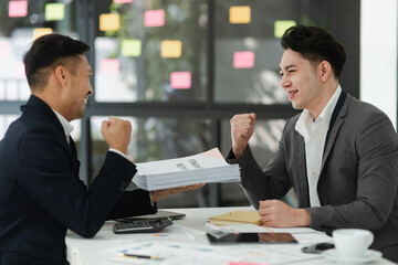 Excited happy young Asian two businessman winner and celebrating success at desk in office.
